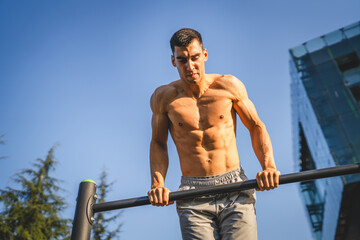 One man muscular male athlete training pull ups outdoor in sunny day