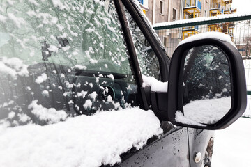 Close-up car rearview mirror with frozen snow. Road safety, challenges and issues with vehicles in snowy, freezing winter weather. Transport, winter concept.