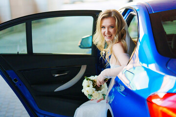 a beautiful and happy bride with a bouquet in a blue car