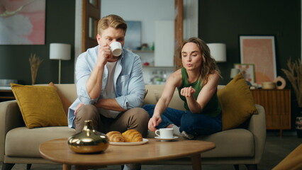 Calm pair talking sofa drinking morning espresso home. Resting woman taking cup