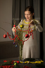 The girl decorates a bouquet of branches with balls and garlands made of natural materials