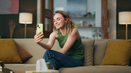 Flirting girl videocalling cellphone sofa. Smiling woman gesturing hands talking