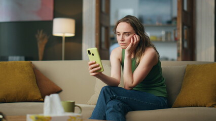 Sad lady using smartphone home sofa. Depressed woman talking video chat indoors