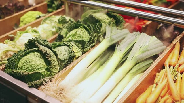 Seasonal leeks, carrots, cabbage are laid out in separate containers on grocery store window. High quality 4k footage