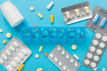 Daily pill organizer with medications on color background, top view
