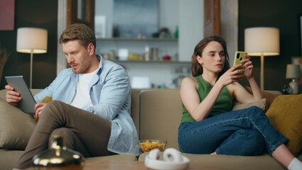 Involved couple reading devices at room. Internet addicted family using gadgets