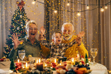 Festive senior couple sitting at cozy home with grandson and celebrating christmas and new year's...