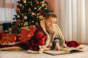 A little boy is reading a book while holding a bunny toy at home on christmas and new year's eve.