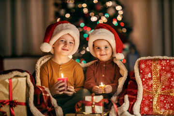 Happy children holding candles at cozy home on christmas eve and smiling at the camera.