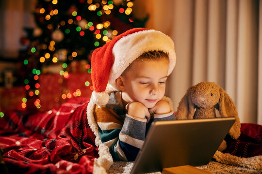 A cute boy is looking at tablet with his bunny toy friend at christmas and new year's eve.