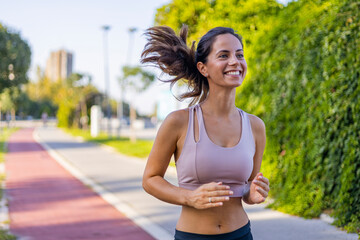 Happy slim woman wearing sportswear jogging in the city at sunrise. Young beautiful female in sports bra running outdoor. Workout exercise in the morning. Healthy and active lifestyle concept.