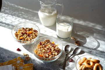 granola with dry fruits, nuts in a transparent bowl, jug and glass with milk, hard light, no people, cozy atmosphere