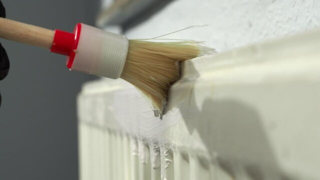 A worker paints a heating radiator with a brush. Heating radiator painting.