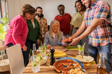 group of multiracial family and friends celebrating birthday at home with a cake with candles. - Powered by Adobe