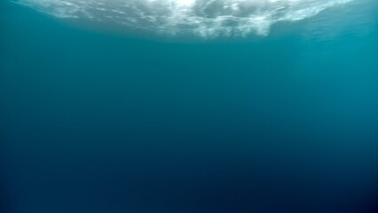 Underwater background of sun shining through water surface and sea waves going past