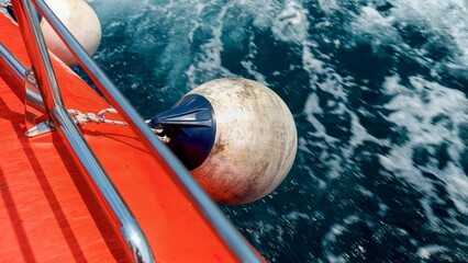 Closeup of fenders and buoys hanging on the side of red rescue boat sailing through cold northern...