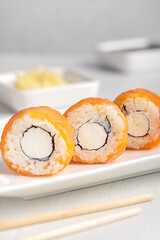 Portion of asian natural tasty philadelphia sushi roll made with raw or smoked salmon fish, cream cheese, nori seaweed and boiled rice served on plate with ginger, soy sauce and bamboo chopsticks