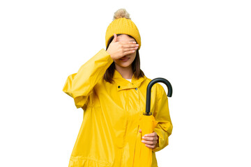 Young Russian woman with rainproof coat and umbrella over isolated chroma key background covering eyes by hands. Do not want to see something