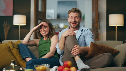 Laughing pair watching comedy sitting home couch. Couple streaming funny movie