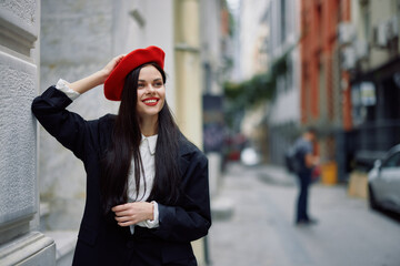 Woman standing near a wall in the city wearing a stylish jacket and red beret with red lips, travel and leisure, French style of dress.