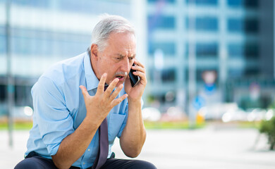 Senior business man yelling at the phone outdoor, sitting on a bench