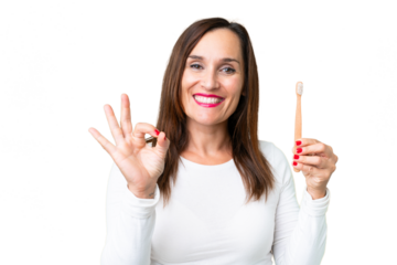 Middle age woman brushing teeth over isolated chroma key background showing ok sign with fingers