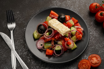 salad of tomatoes, cucumbers, red onions and feta cheese on a black plate, dark gray background, no people, close-up