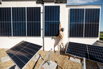 Man installing solar panels on vertical wall on a rooftop of his house for self consumption. Renewable energy and sustainability concept - obrazy, fototapety, plakaty