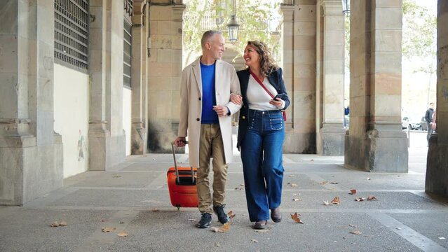 Portrait of a happy mature couple sightseeing on a romantic journey trip in Spain. Middle aged married people walking with a suitcase. Wife and husband smiling and having fun on a weekend tour. High