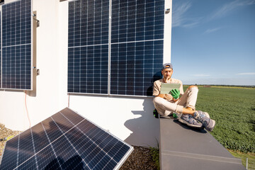 Man sitting on a rooftop and using digital tablet monitoring production from the solar power...