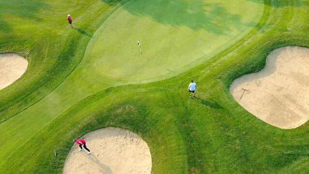 Top view of a golf course on a sunny day with golfers on the course. Three golfers with clubs on a green golf course. Aerial view.