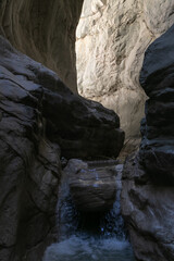 A narrow passage among steep cliffs in a mountain gorge. A swift mountain stream flows at the bottom of the gorge. Fascinating trekking in the mountain park of Saklikent Canyon.
