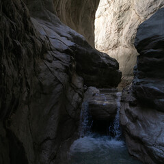 A narrow passage among steep cliffs in a mountain gorge. A swift mountain stream flows at the bottom of the gorge. Fascinating trekking in the mountain park of Saklikent Canyon.