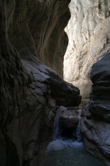 A narrow passage among steep cliffs in a mountain gorge. A swift mountain stream flows at the bottom of the gorge. Fascinating trekking in the mountain park of Saklikent Canyon.