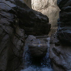 A narrow passage among steep cliffs in a mountain gorge. A swift mountain stream flows at the bottom of the gorge. Fascinating trekking in the mountain park of Saklikent Canyon.