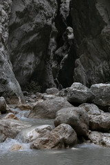 A narrow passage among steep cliffs in a mountain gorge. A swift mountain stream flows at the bottom of the gorge. Fascinating trekking in the mountain park of Saklikent Canyon.