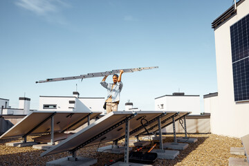 Man carries ladder during solar panels installation on a rooftop of a private house on a sunny day....