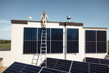 Rooftop of a private house with solar power station on it, man sitting on a top and enjoys his...