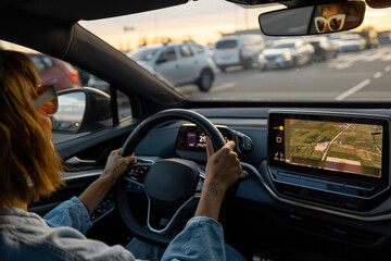 Woman drives modern electric car on a highway with lots of cars at sunset. Concept of modern...