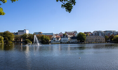 Fototapeta na wymiar Panoramic photography in Stavanger, the artificial lake called Breiavatnet, with a fountain in its central part and beautiful old buildings around it. Norway
