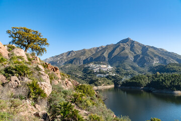 a view from a cliffside overlooking a reservoir and pueblo Blanco at the foot of a mountain along the Costa Del Sol. 