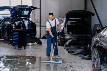 Handsome positive car mechanic repair service center cleaning using mops to roll water from the...