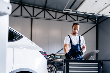 Portrait of automotive technician at auto service center. Auto mechanic using computer software for diagnostics engine working and repairing car in a garage.