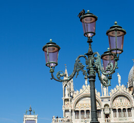 Close-up of a streetlight in St. Mark's Square in Venice against the blue sky. In the background is...