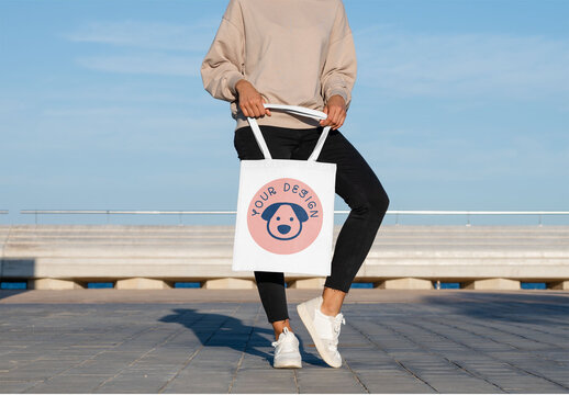 Mockup of woman holding customizable tote bag bending one leg, low section