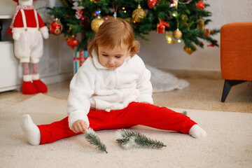 Adorable little girl having fun on a soft carpet in front of a Christmas tree