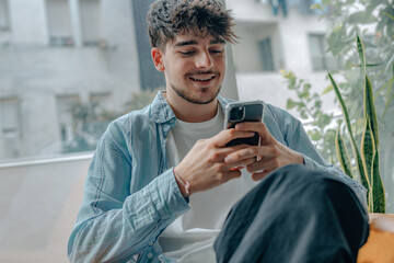 young man with mobile phone sitting on the sofa at home - obrazy, fototapety, plakaty
