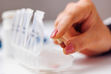 Woman hand taking pill from pillbox or organizer for daily medication