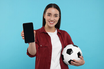 Happy fan holding soccer ball and showing smartphone on light blue background