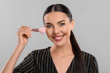 Everyday makeup. Beautiful woman applying face powder on light grey background